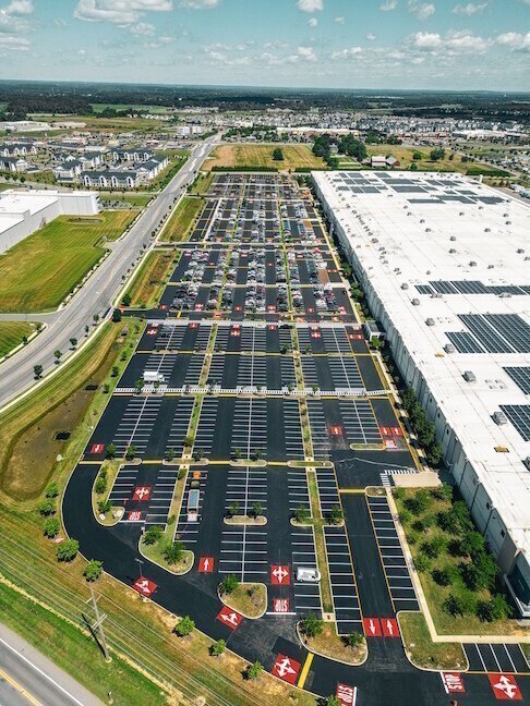 Aerial view of a large warehouse building and its massive, freshly paved parking lot featuring bright red directional markings.